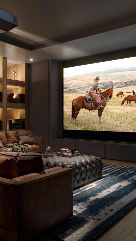 A luxurious home theater featuring a large screen displaying a cowboy on horseback in a grassy field, with comfortable seating and warm, ambient lighting.