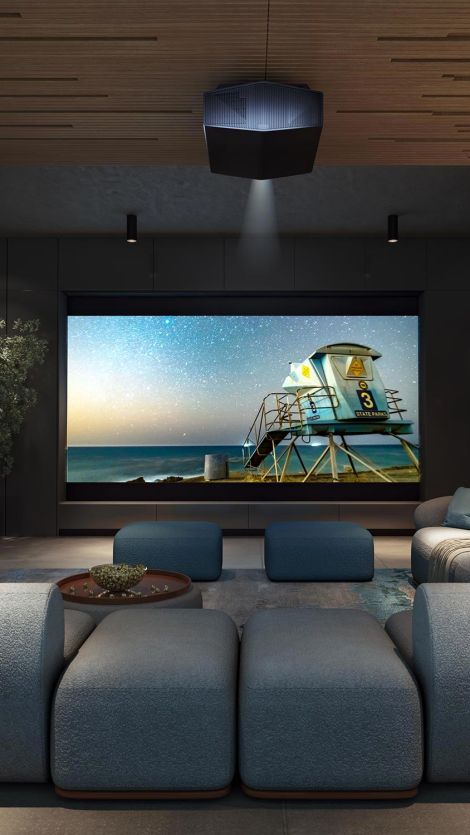 A modern home theater with a large screen showing a lifeguard tower on a beach at sunset, surrounded by cozy seating and dim lighting.