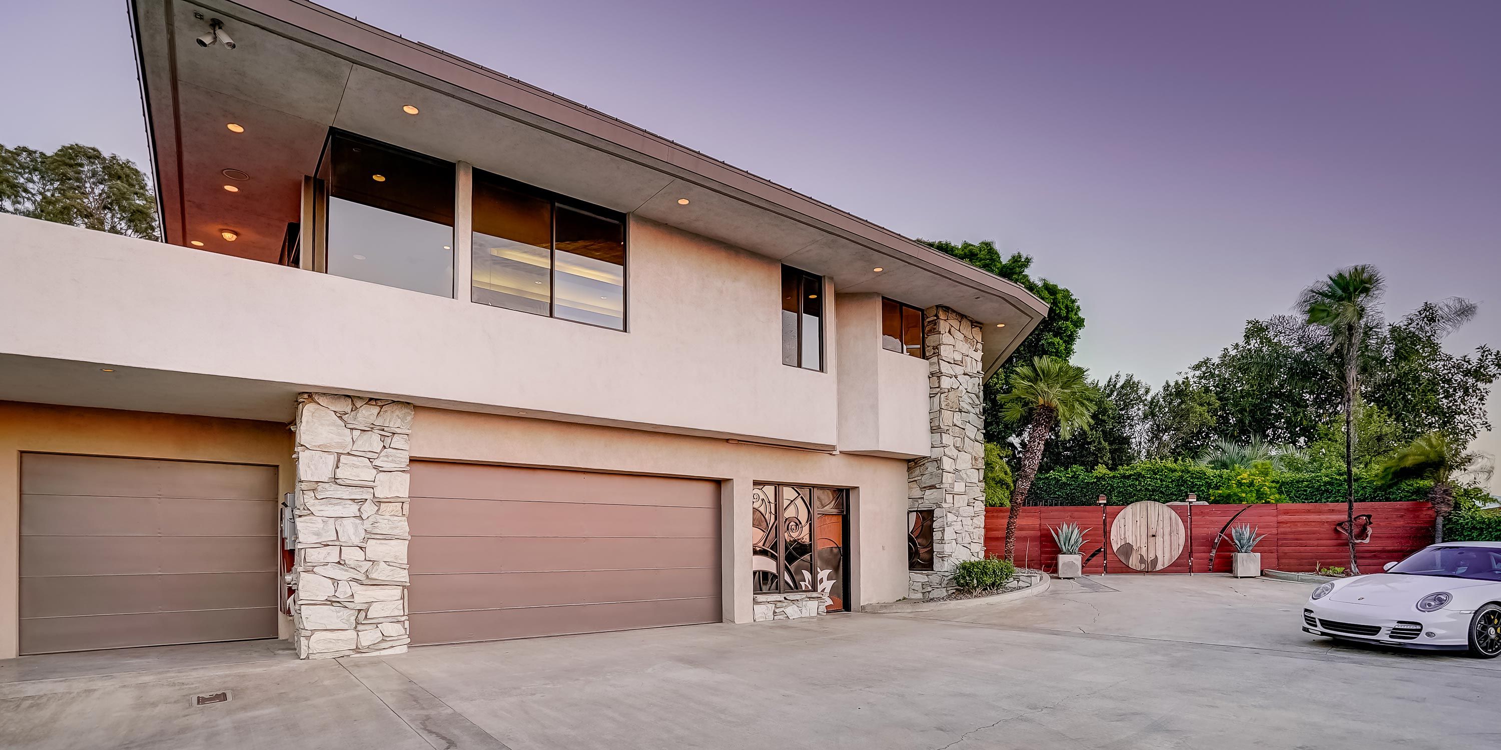 A sleek, modern house with stone accents and a gated driveway, featuring a sports car parked in front.