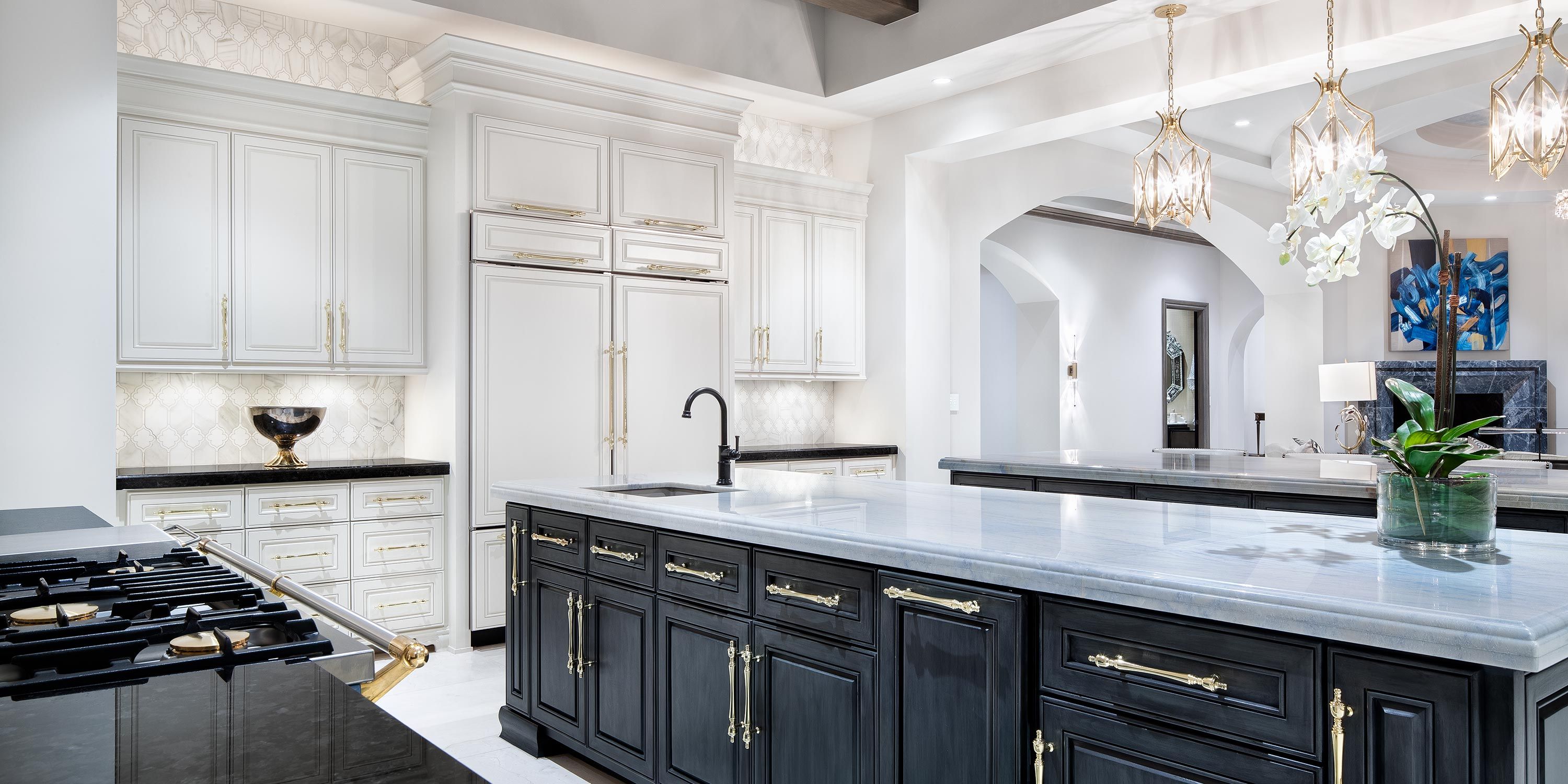 A luxurious kitchen with white cabinetry, a large island with dark cabinets, elegant gold hardware, and sophisticated lighting fixtures, featuring a modern and bright design.
